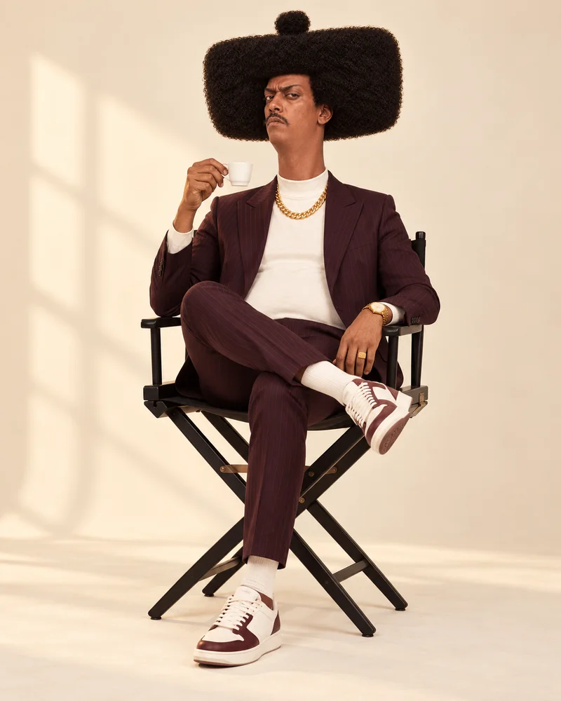 Phil Jean in his burgundy suit, holding a tiny espresso in a director’s chair. Big hair. Unimpressed expression.
