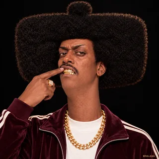 Phil in a tight front-facing portrait, lifting his upper lip with one finger to reveal immaculate gold grillz, raised skeptical eyebrow, burgundy tracksuit jacket, heavy gold chain, harsh on-camera flash, black background. Hilariously serious, understated flex.