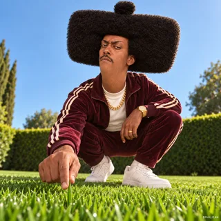 Phil crouching in an immaculate bright green lawn, touching one blade of grass with his index finger while staring suspiciously at it as if he has never seen it, expensive burgundy tracksuit and white trainers, wide low angle.